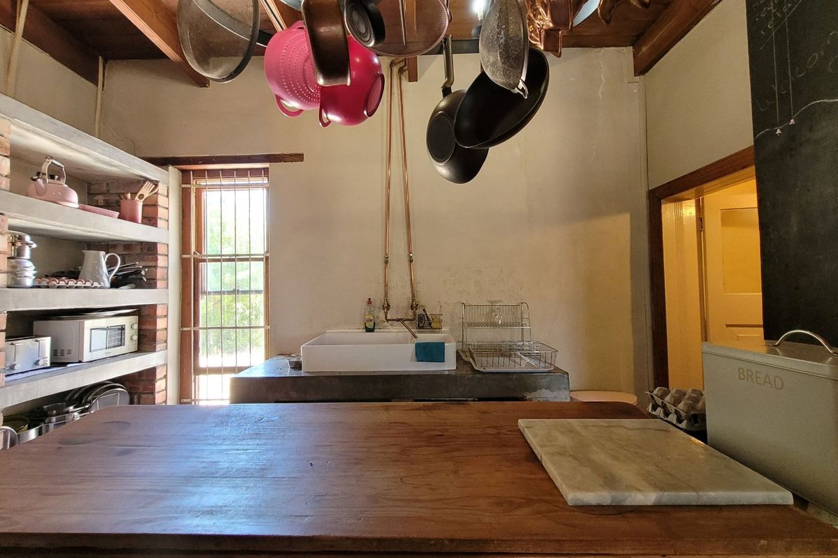 Rustic kitchen featuring exposed timber beams, brick shelving, a concrete countertop with a farmhouse sink, and exposed copper plumbing details.