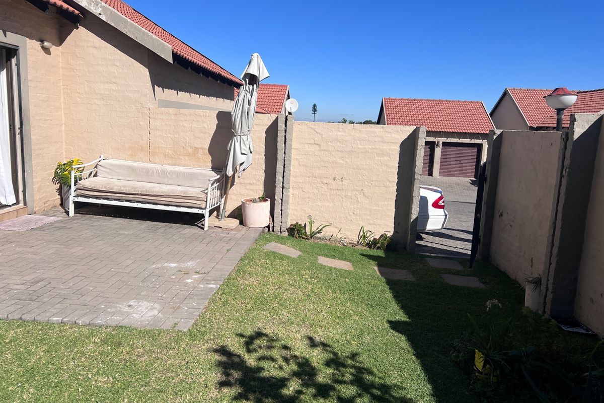 A private rear courtyard featuring a paved patio area, a small lawn, and a boundary wall with access to the driveway.