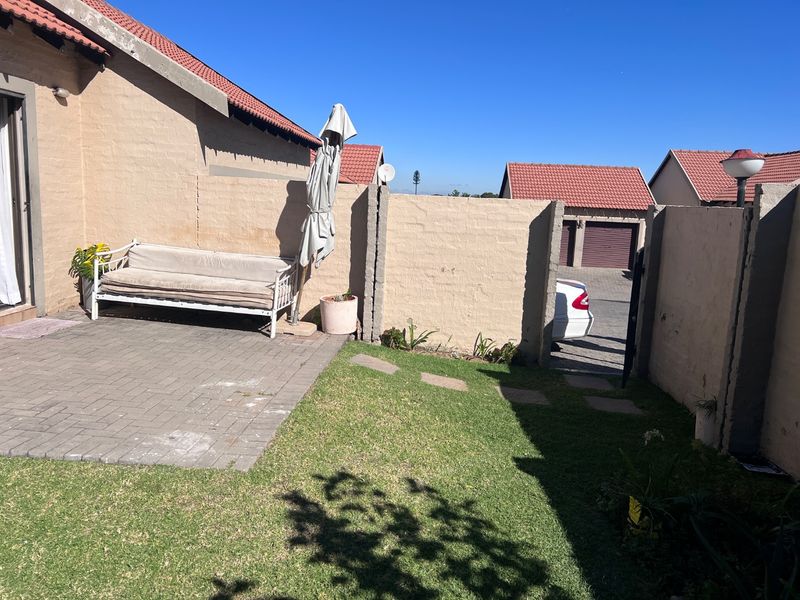 A private rear courtyard featuring a paved patio area, a small lawn, and a boundary wall with access to the driveway.