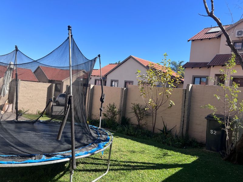 A private rear garden area featuring a lawn, paved section, and perimeter boundary walls within a townhouse complex.