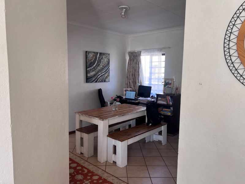 A functional living area featuring tiled flooring and a window with security bars, currently utilized as a combined dining and workspace.