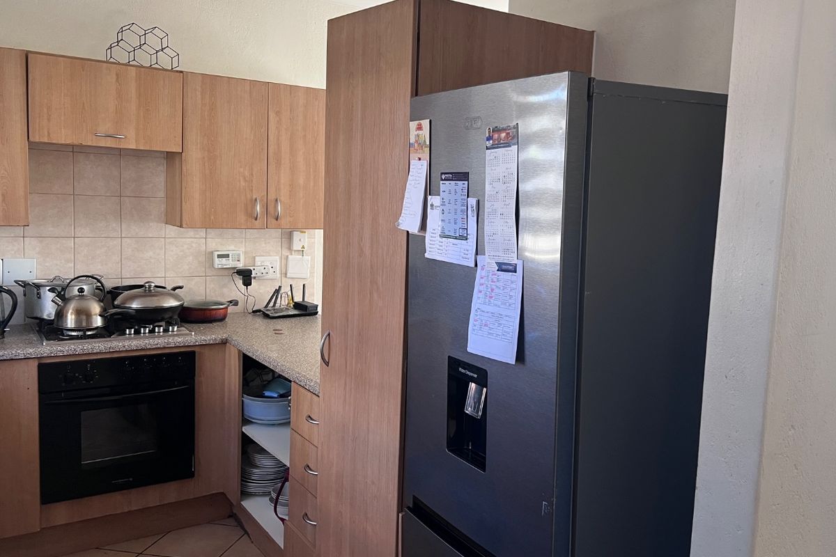 A functional kitchen featuring light wood-finish cabinetry, laminate countertops, a built-in oven with gas hob, and tiled flooring.