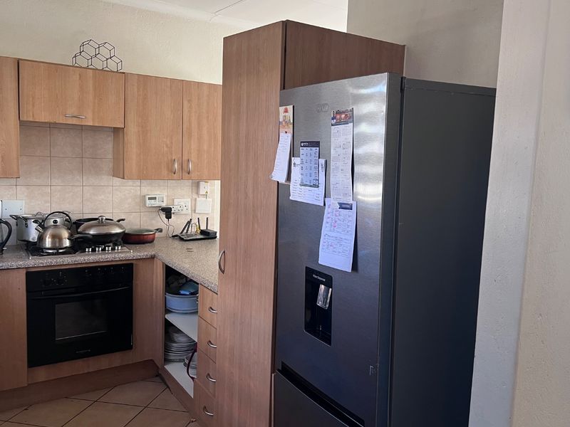 A functional kitchen featuring light wood-finish cabinetry, laminate countertops, a built-in oven with gas hob, and tiled flooring.