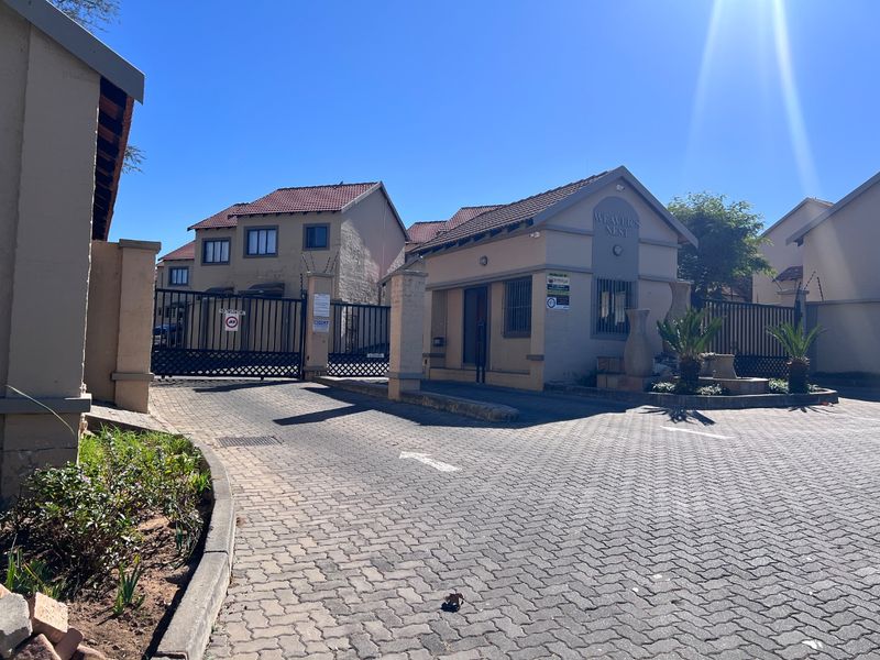 Front entrance view of the Weaver's Nest townhouse complex, featuring a secure gated access point, paved driveway, and guard house.