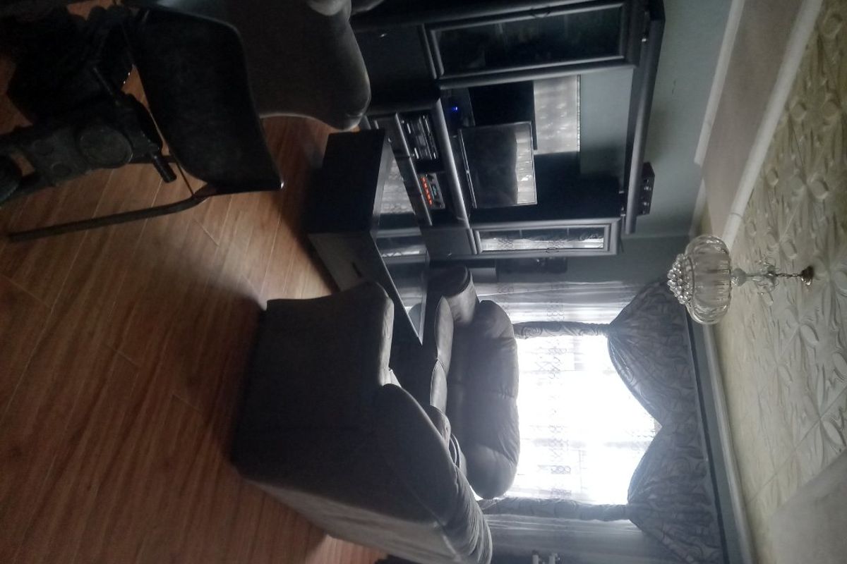 A living room featuring laminate flooring and decorative ceiling tiles, providing a functional space for relaxation.