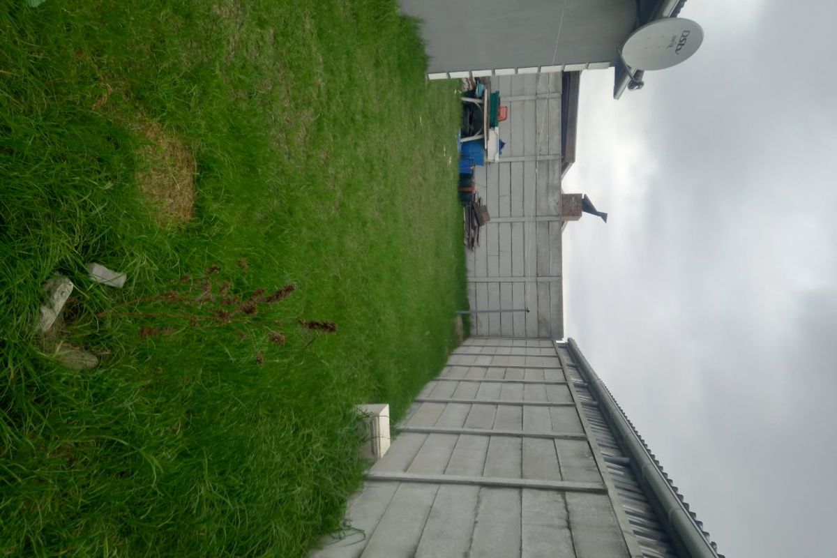 A rear garden area featuring a lawn enclosed by precast concrete boundary walls and a mounted satellite dish.
