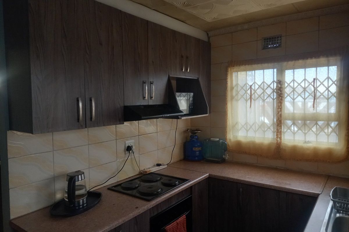 A functional kitchen featuring dark wood-look cabinetry, laminate countertops, an electric hob, and a tiled backsplash with a security-fitted window.