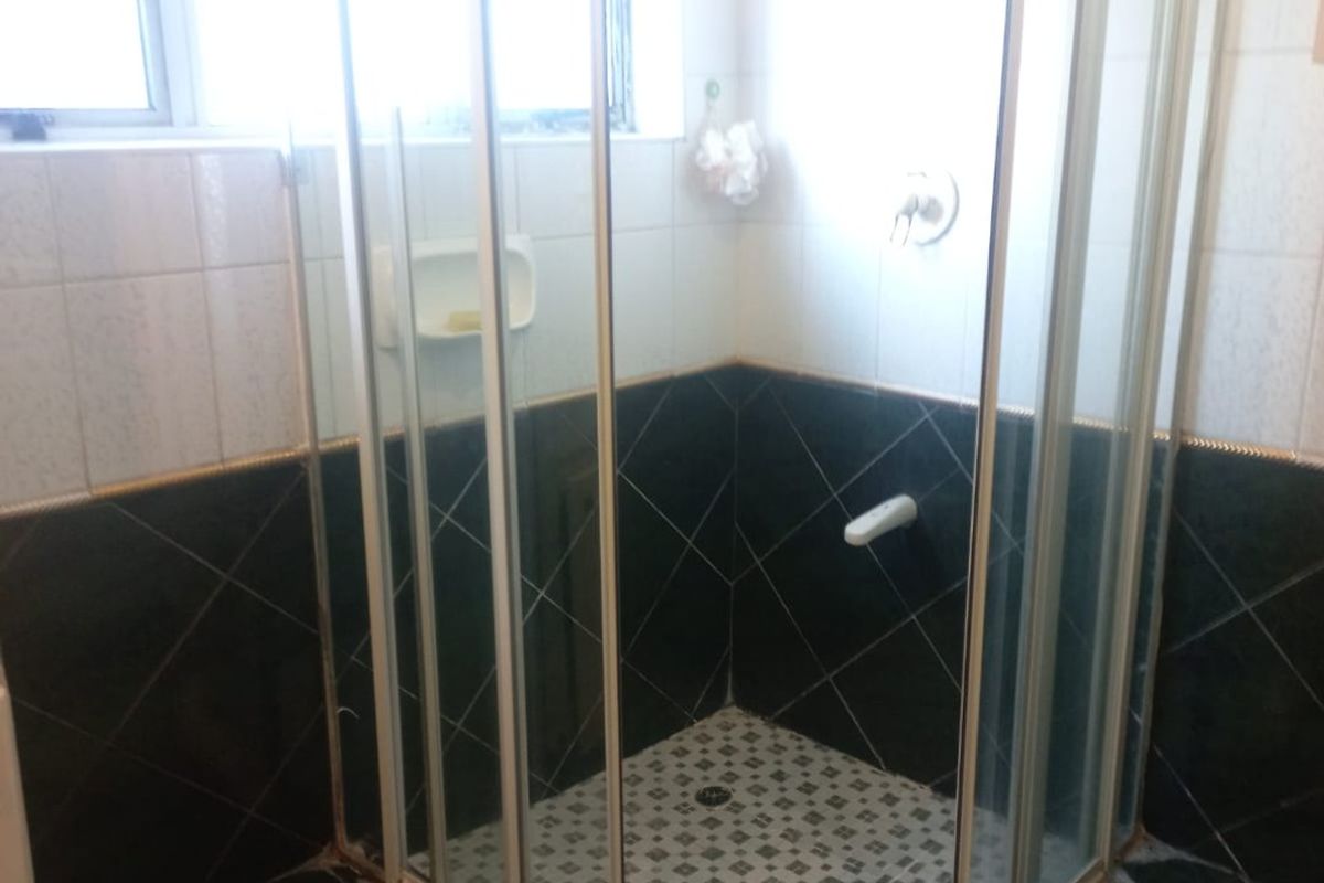 A bathroom featuring a corner shower enclosure with dark tiled walls and flooring, requiring minor maintenance and cosmetic updates.