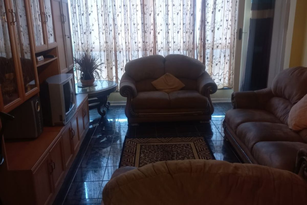 A living room featuring dark tiled flooring, a ceiling fan, and a large window with curtains, providing natural light to the space.