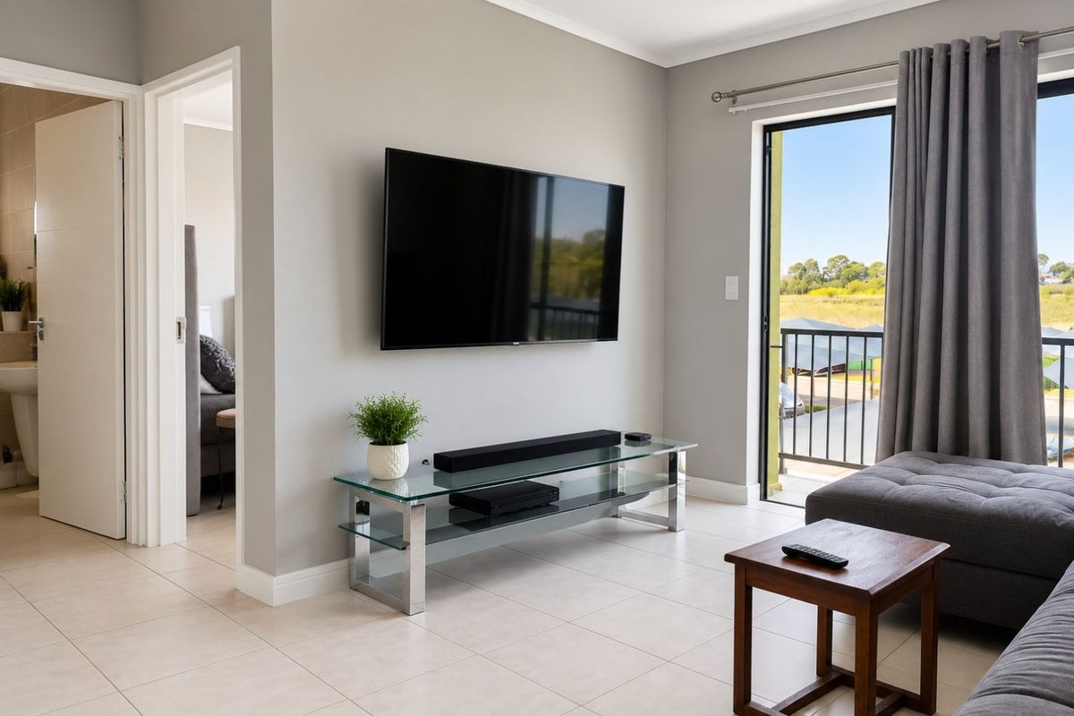 A bright, modern living room featuring neutral tiled flooring, coving, and direct access to a balcony through a sliding glass door.