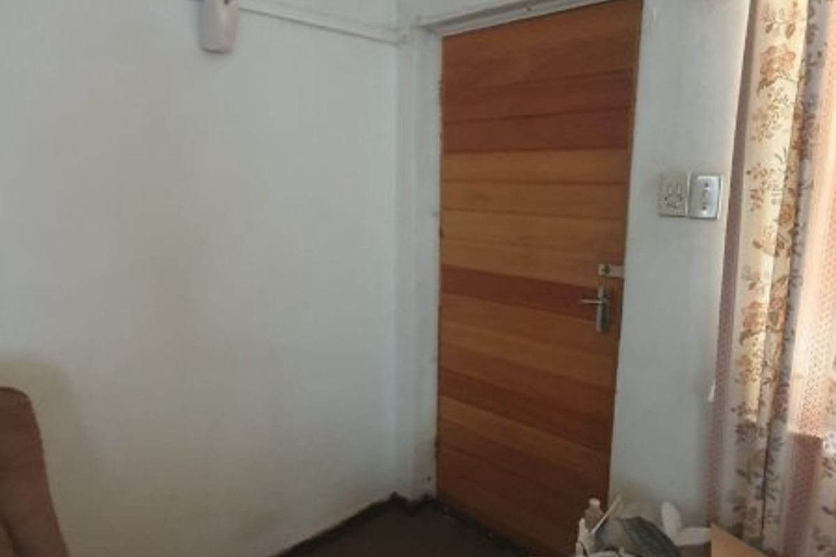 A bedroom interior featuring a wooden door, coving, and electrical fixtures, currently showing signs of wear and requiring cosmetic updates.