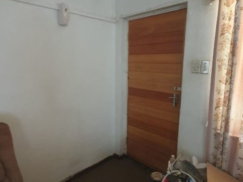 A bedroom interior featuring a wooden door, coving, and electrical fixtures, currently showing signs of wear and requiring cosmetic updates.