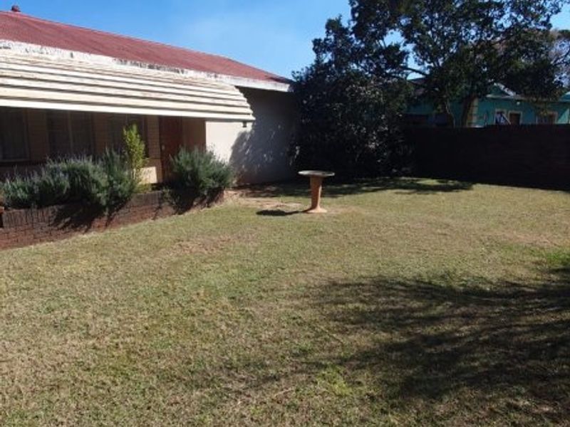 A spacious rear garden featuring a lawn, brick planter box, and a house exterior with a metal roof and window awning.