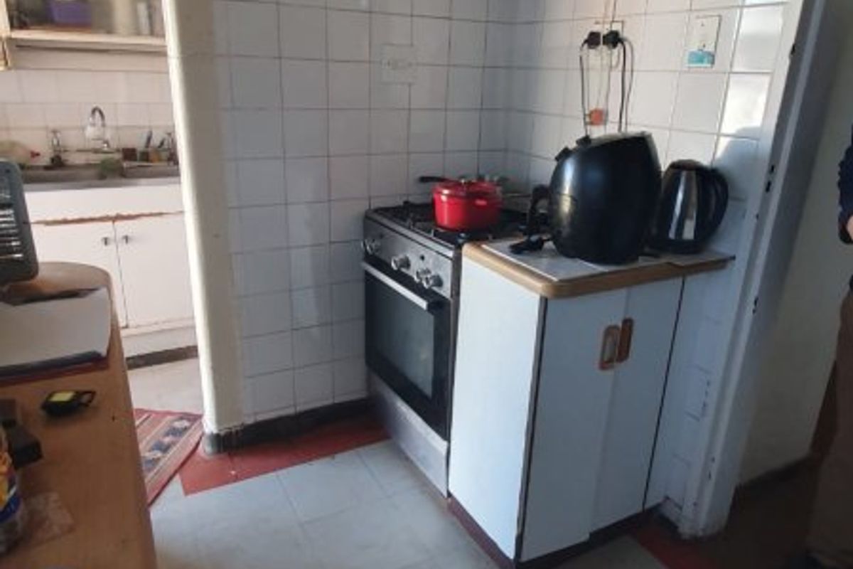 A compact, dated kitchen featuring a built-in oven, gas hob, extractor fan, and tiled splashback, with an adjacent scullery area visible.