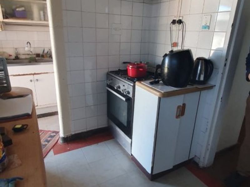 A compact, dated kitchen featuring a built-in oven, gas hob, extractor fan, and tiled splashback, with an adjacent scullery area visible.