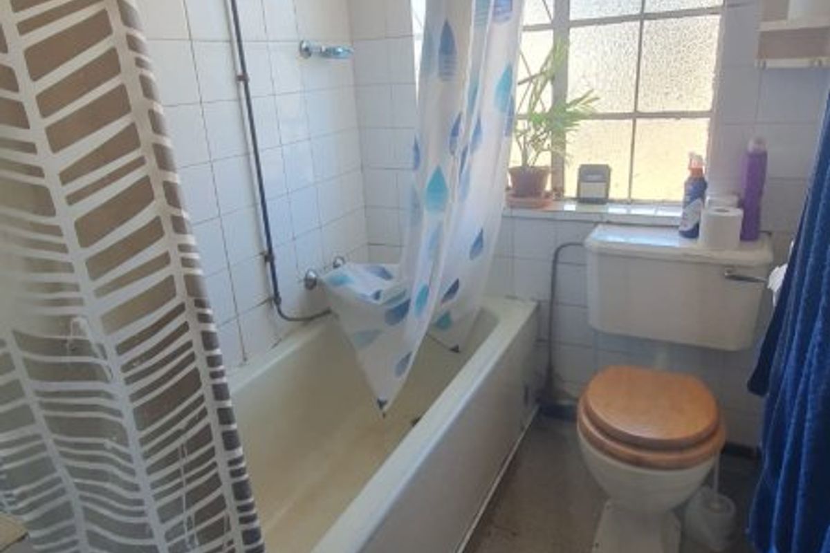 A functional bathroom featuring a bathtub with an overhead shower, a standard toilet, and tiled wall finishes, requiring cosmetic updates.