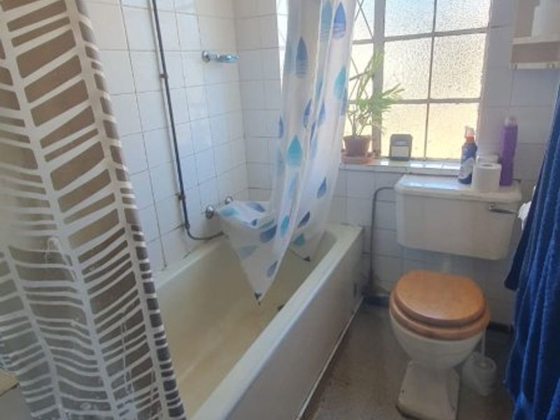 A functional bathroom featuring a bathtub with an overhead shower, a standard toilet, and tiled wall finishes, requiring cosmetic updates.