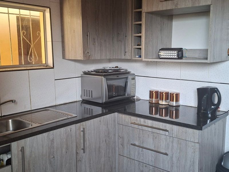 A functional kitchen featuring wood-look laminate cabinetry, dark granite countertops, a stainless steel sink, and tiled splashbacks with security bars on the window.