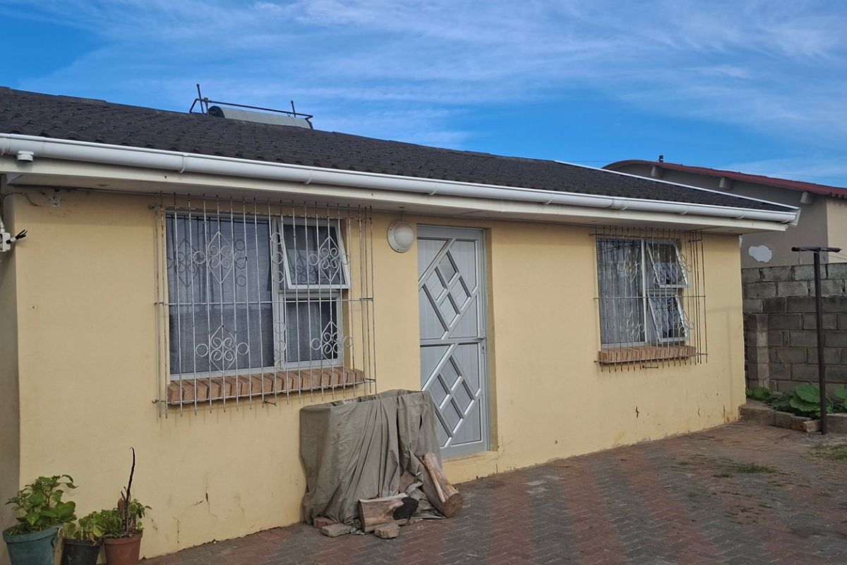 Rear exterior view of the house featuring a paved courtyard, security bars on windows, and a solar water heater installed on the tiled roof.