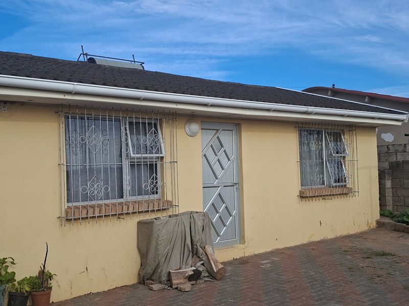 Rear exterior view of the house featuring a paved courtyard, security bars on windows, and a solar water heater installed on the tiled roof.