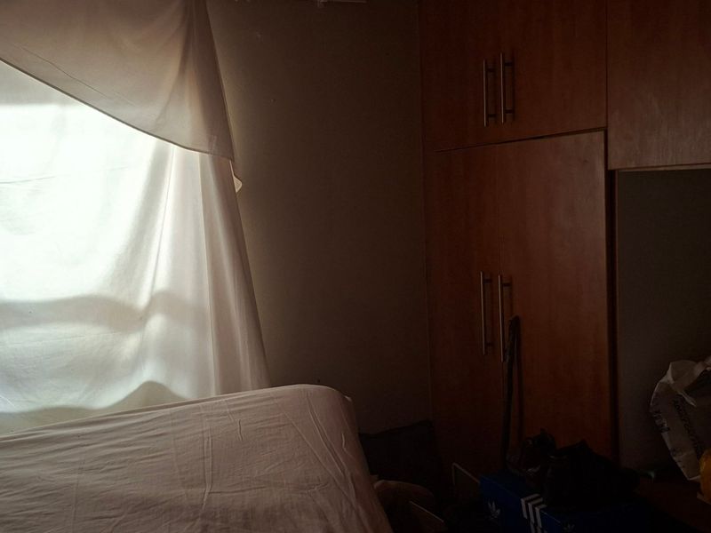 A bedroom featuring built-in wooden cupboards and a window with natural light, currently in need of maintenance and improved lighting.