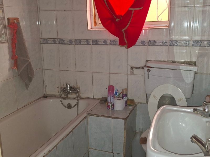 A dated bathroom featuring a standard bathtub, pedestal basin, and toilet with tiled finishes, requiring renovation to update the fixtures and wall surfaces.