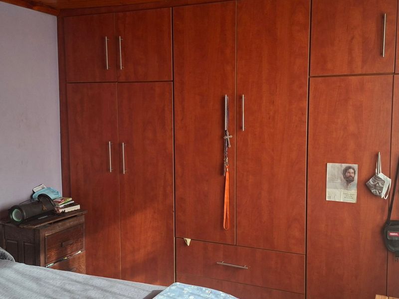 A bedroom featuring floor-to-ceiling built-in wooden cupboards with modern handles and warm timber ceiling detailing.