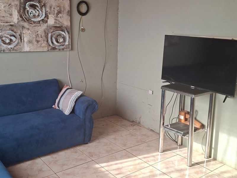 A living room area featuring ceramic floor tiles and wall-mounted electrical points, currently requiring cosmetic updates to the wall finishes and trim.