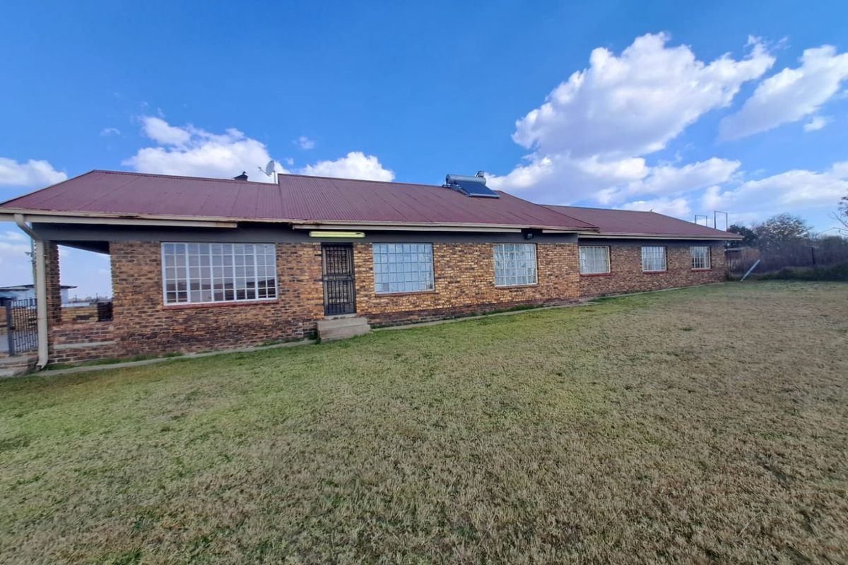 Rear view of a single-story face brick farmhouse featuring a corrugated metal roof with an integrated solar water heating system.