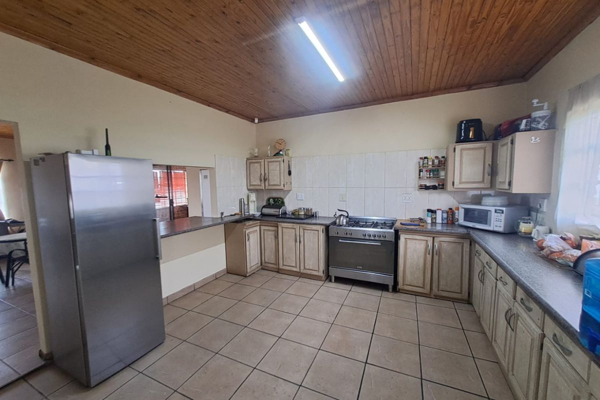 A functional kitchen featuring wooden ceilings, tiled flooring, built-in cabinetry, and a gas stove with a breakfast counter pass-through to the adjacent living area.