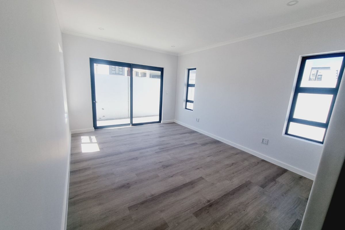 A bright, modern, and empty living room featuring neutral walls, wood-look laminate flooring, and large sliding glass doors leading to the exterior.