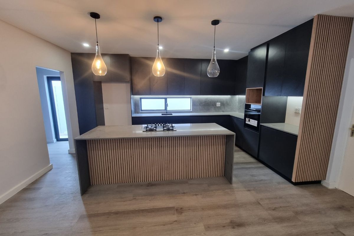 Modern kitchen featuring sleek black cabinetry, a central island with a gas cooktop, stone countertops, and stylish slatted wood accents.