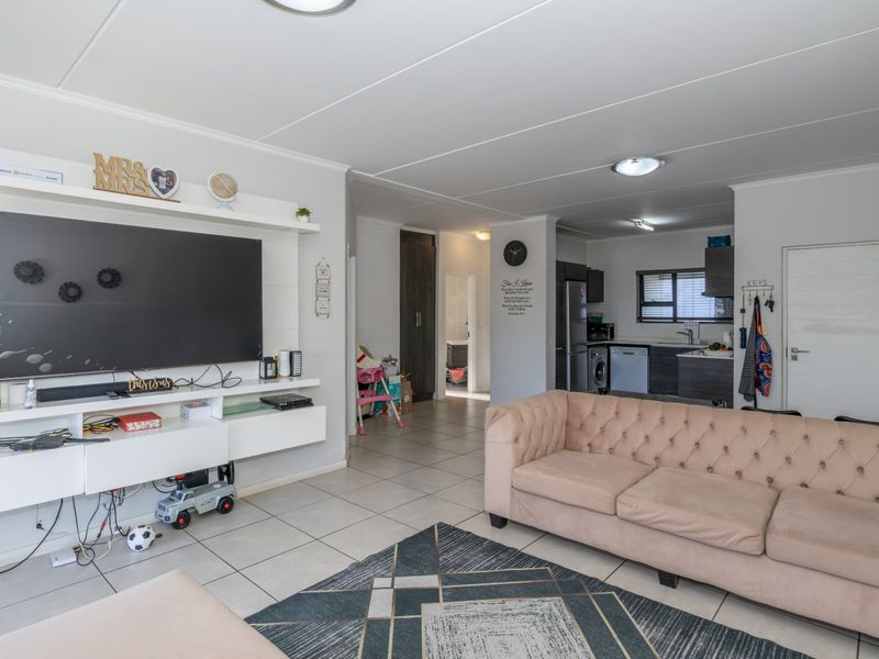 Open plan living area featuring tiled flooring, a built-in media console, and an integrated kitchen space with cabinetry.
