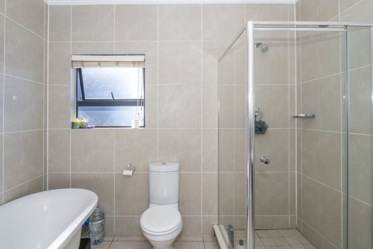 A well-maintained bathroom featuring a freestanding bathtub, a separate glass-enclosed shower, a toilet, and neutral floor-to-ceiling wall tiling.