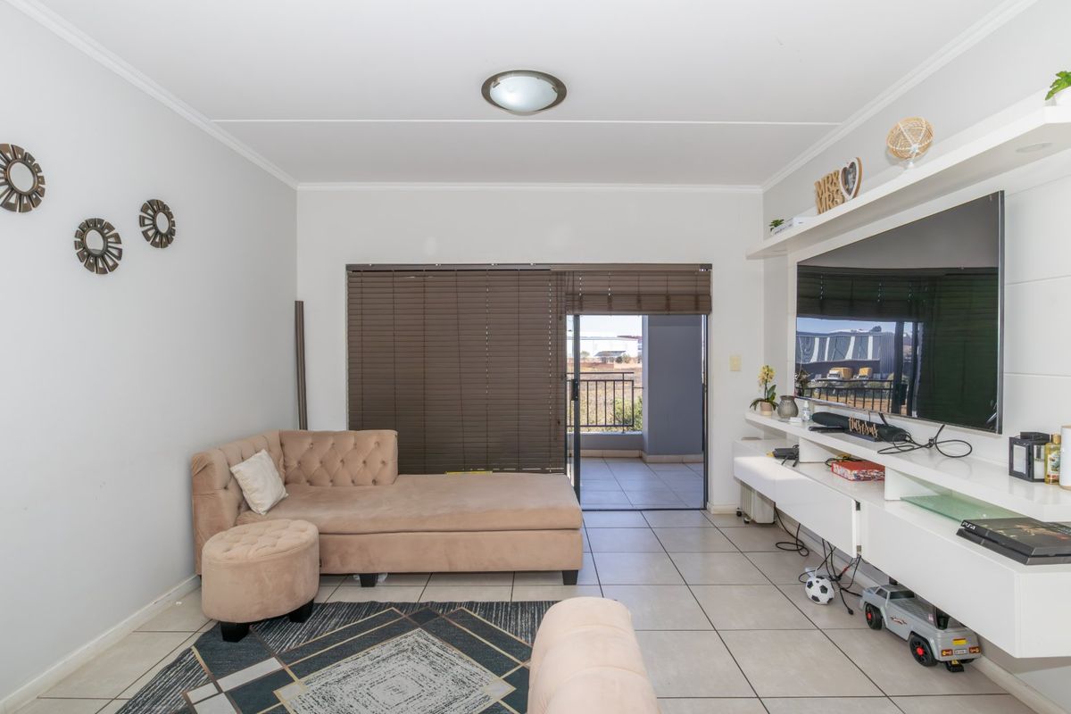 A bright living room featuring tiled flooring, a built-in media console, and a sliding glass door providing access to an outdoor balcony.