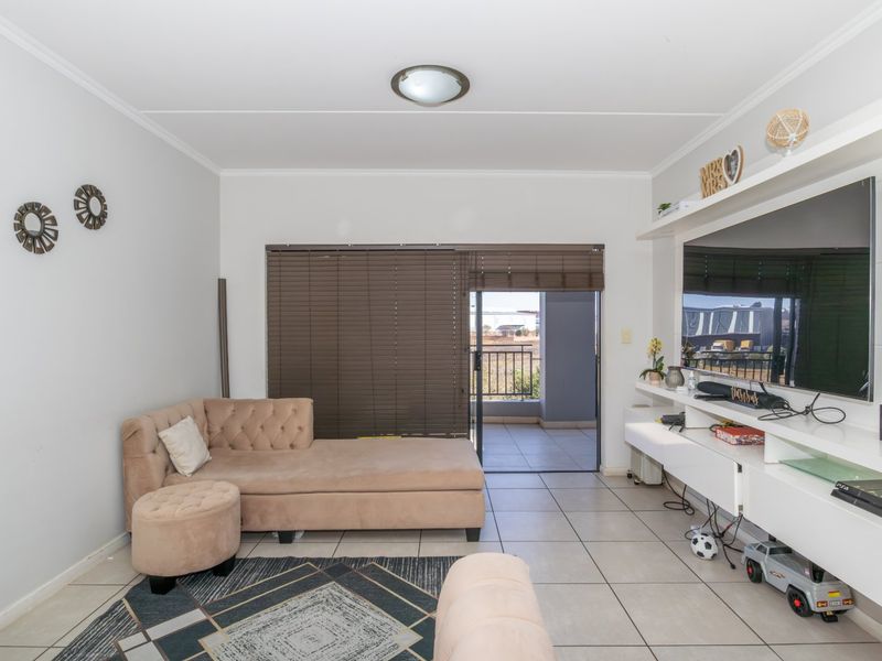 A bright living room featuring tiled flooring, a built-in media console, and a sliding glass door providing access to an outdoor balcony.