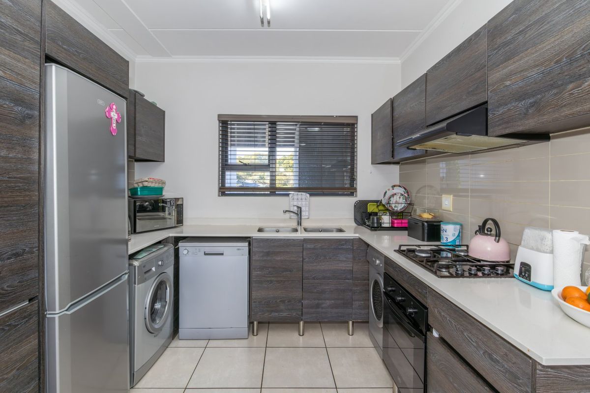 A functional kitchen featuring dark wood-grain cabinetry, stone-look countertops, a gas hob, built-in oven, and integrated space for laundry appliances.