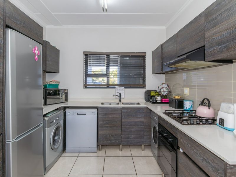 A functional kitchen featuring dark wood-grain cabinetry, stone-look countertops, a gas hob, built-in oven, and integrated space for laundry appliances.