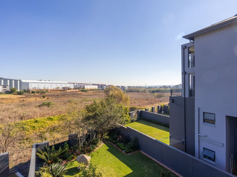 Elevated view overlooking a landscaped garden, boundary wall, and open field landscape from the apartment balcony.