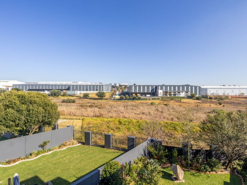 Elevated view overlooking a landscaped garden, boundary wall, and open field with industrial buildings in the distance.