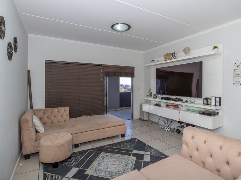 A well-maintained living room featuring tiled flooring, a built-in media console, and direct access to an outdoor balcony through a sliding door.