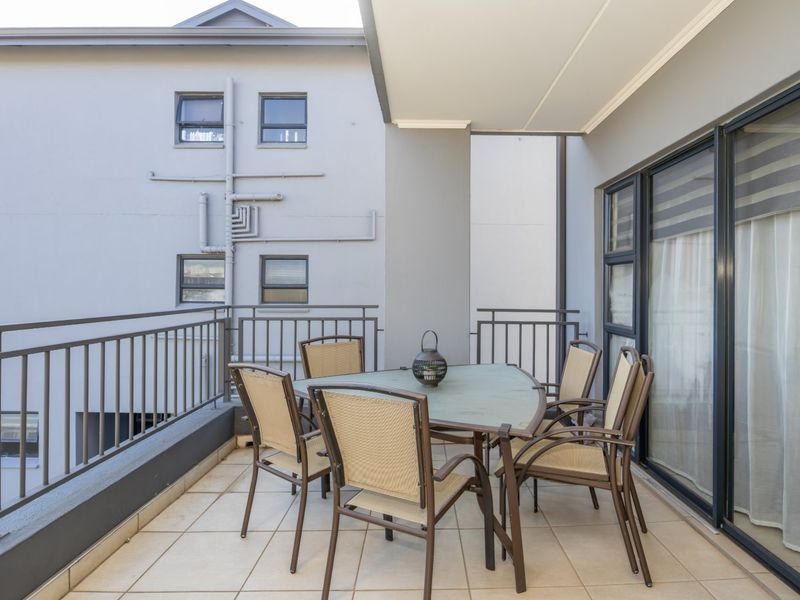 A covered balcony featuring tiled flooring and metal railings, providing an outdoor space accessible through large sliding glass doors.