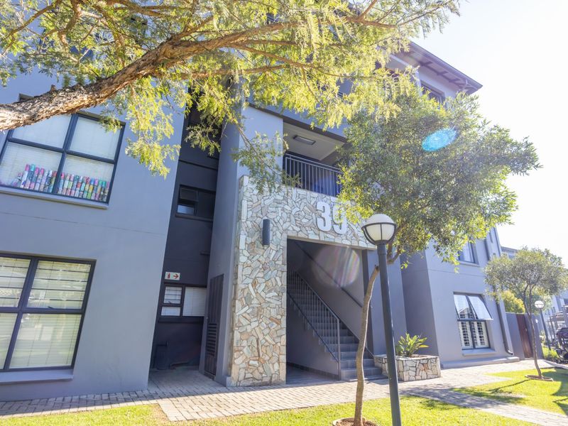 Front elevation of a modern apartment building featuring stone cladding, a central staircase, and paved walkways with landscaped surroundings.