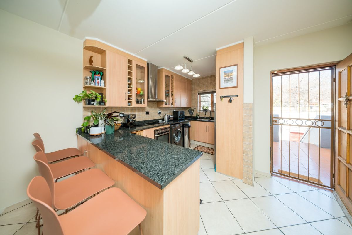 Functional kitchen featuring granite countertops, built-in cabinetry, integrated appliances, and direct access to an outdoor patio area through a security gate.