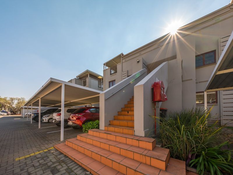 Exterior view of the townhouse complex featuring covered parking bays, paved driveway, and an external staircase leading to upper-level units.