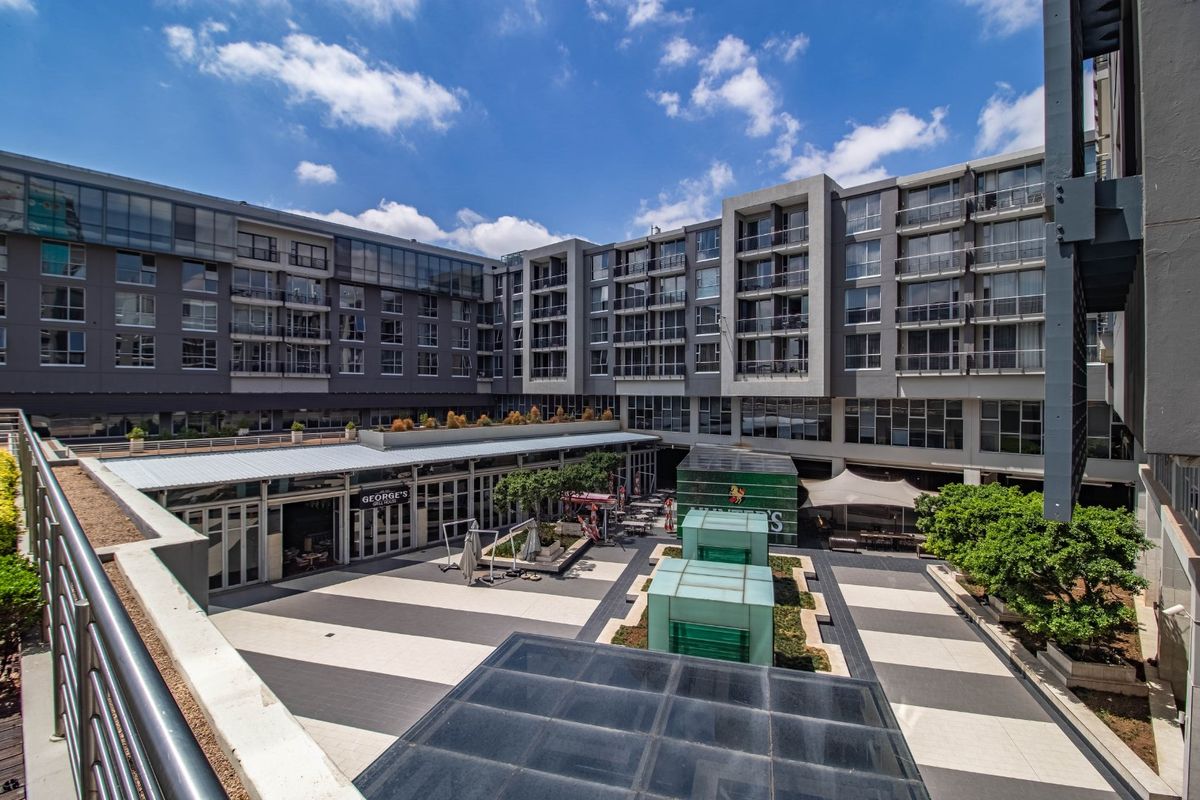 An elevated view of a modern apartment complex courtyard featuring paved walkways, glass skylights, and surrounding residential balconies.