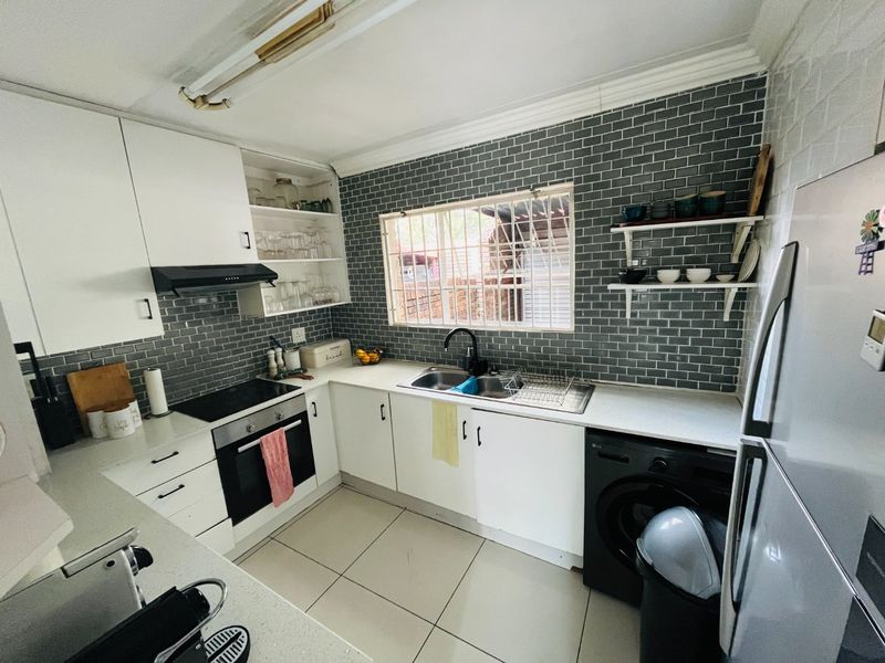 A functional kitchen featuring white cabinetry, a grey subway tile backsplash, built-in oven and hob, and a double basin sink with a window view.