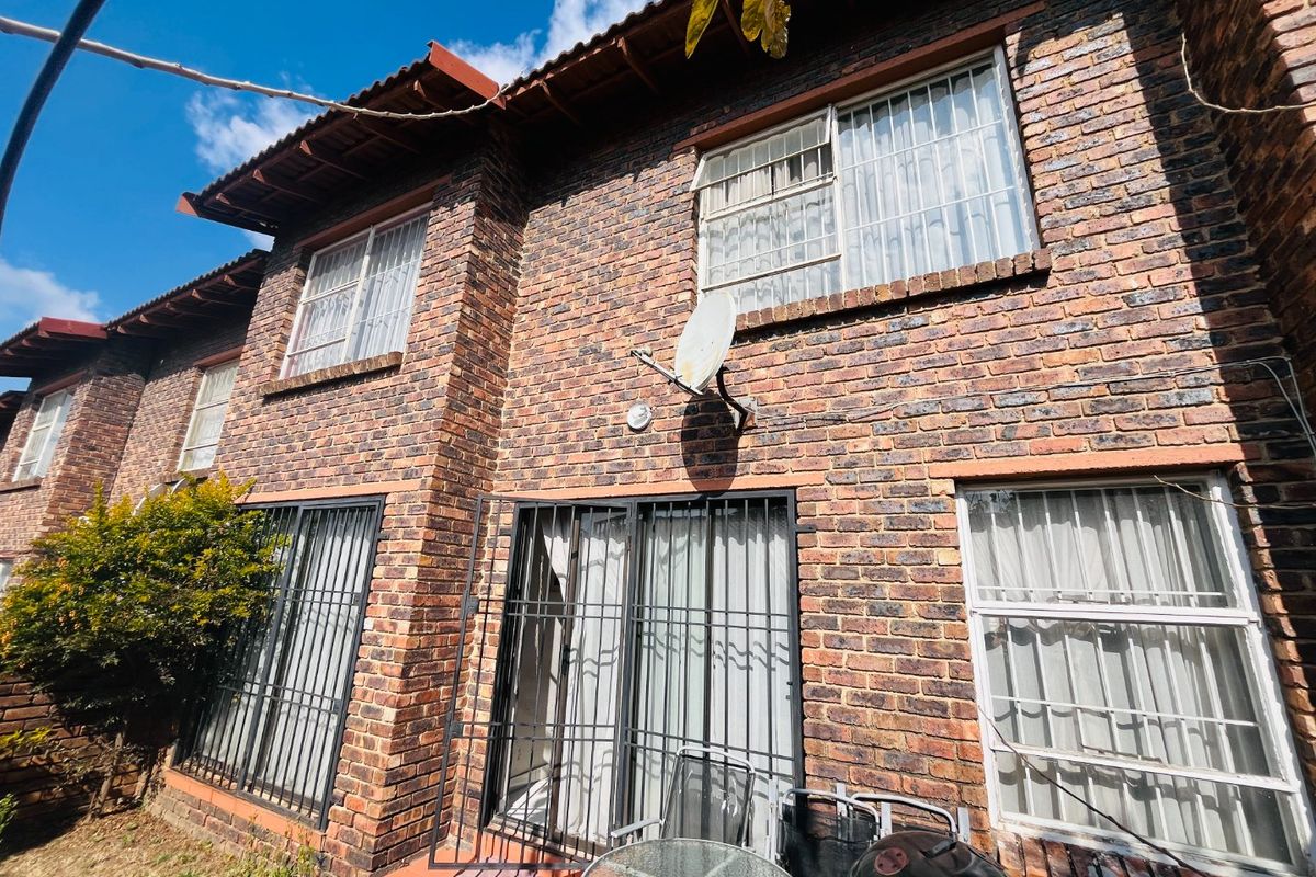 Rear elevation of a double-story townhouse featuring face brick construction, tiled roofing, and security bars on windows and doors.