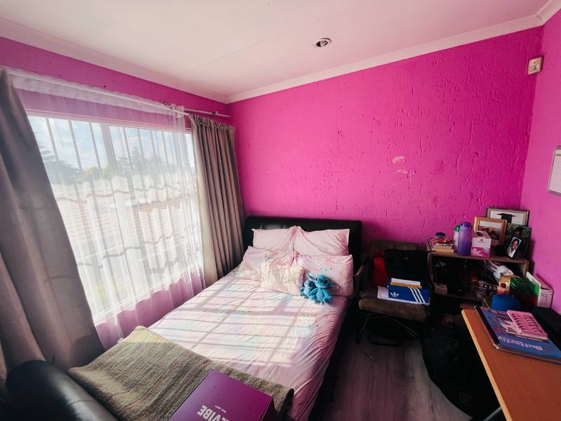 A bedroom featuring laminate flooring and recessed ceiling lighting, currently finished with bright pink textured walls that show signs of wear.