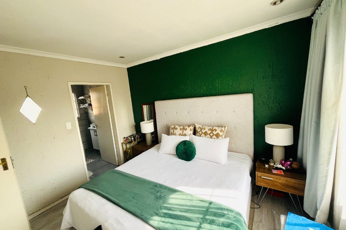 A bedroom featuring a bold green accent wall, recessed lighting, and laminate flooring, with an adjoining space visible through the doorway.